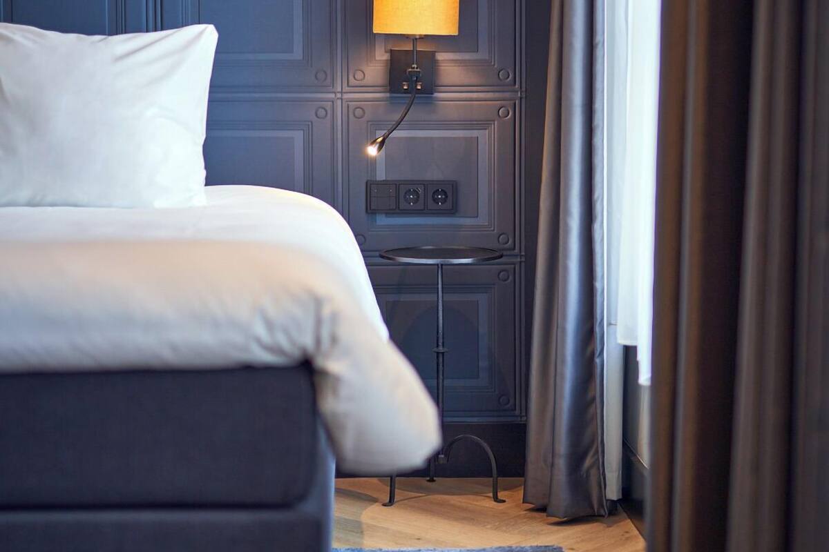 Habitación de hotel moderna con una cama grande, una mesita de noche, una lámpara y vistas al exterior.
