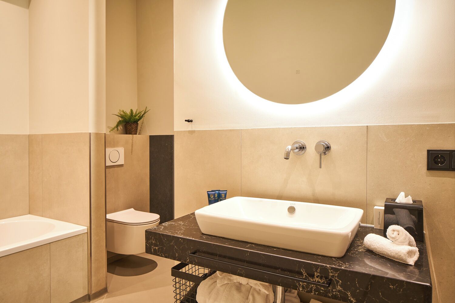 A modern bathroom with a large oval mirror, a white sink, and a toilet.