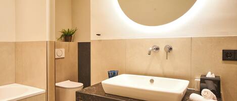 A modern bathroom with a large oval mirror, a white sink, and a toilet.