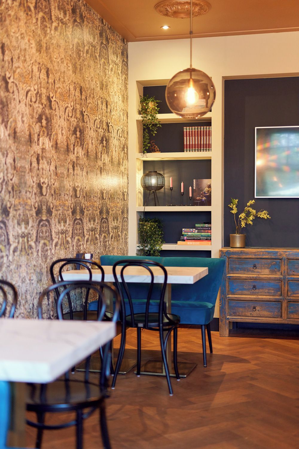 Un comedor con mesa y sillas de madera, una estantería con libros y objetos decorativos, y una pared con un diseño texturizado.