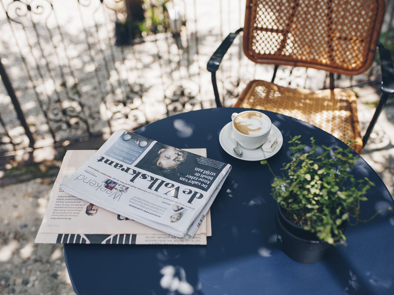 A round table with a newspaper, a cup of coffee, and a small potted plant.