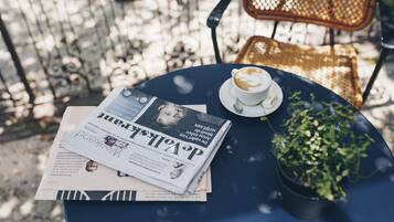 A round table with a newspaper, a cup of coffee, and a small potted plant.