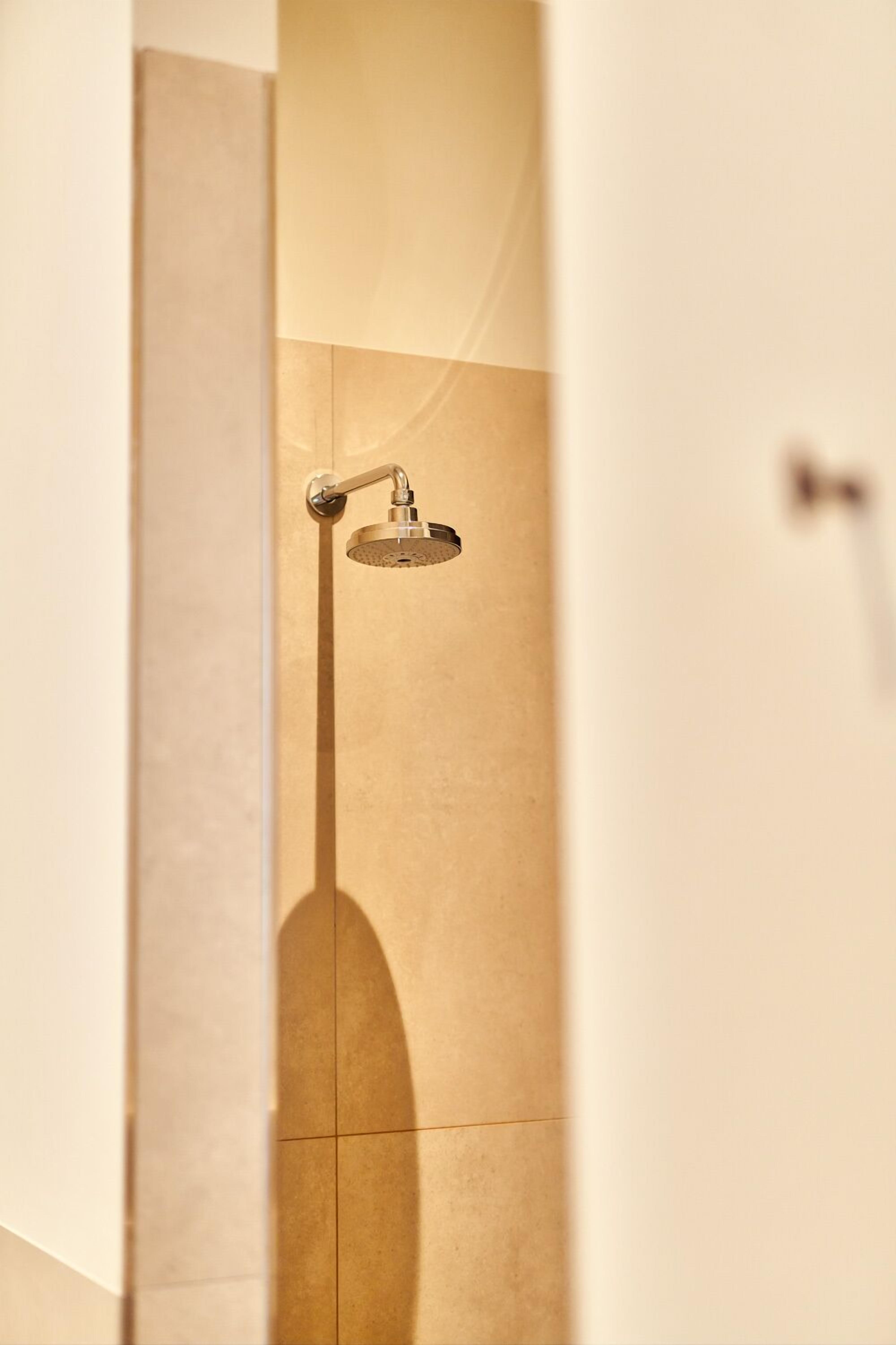 A bathroom with a shower head mounted on a wall, a door, and a tiled floor.