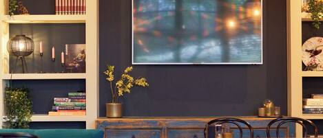 A modern dining area with a dark wall, a flat-screen TV, and blue upholstered chairs.