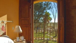 Una habitación con una cama, una mesita de noche con lámpara y vista a un jardín por una puerta abierta.
