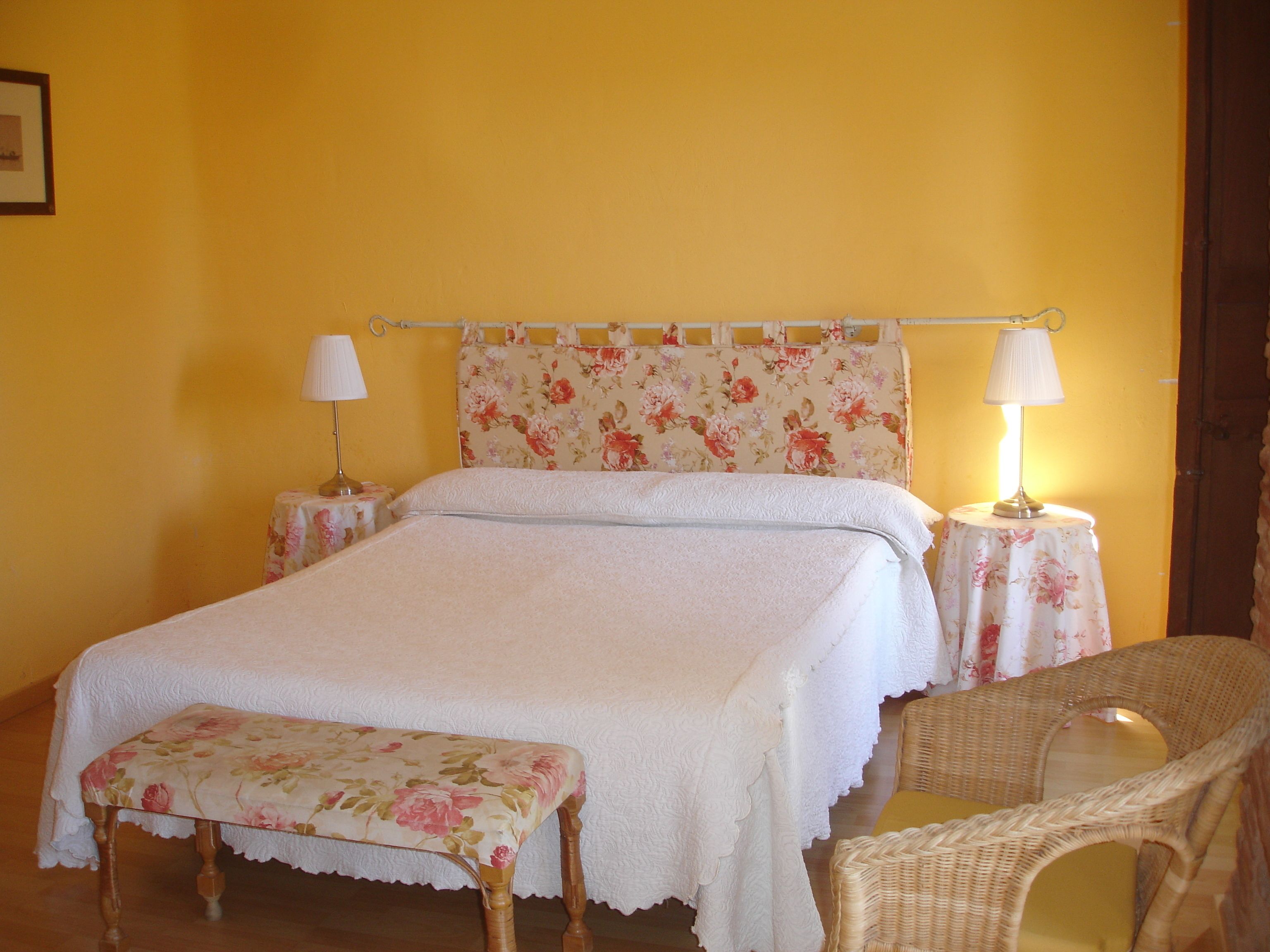 A bedroom with a bed, two bedside tables with lamps, a bench, and a wicker chair.