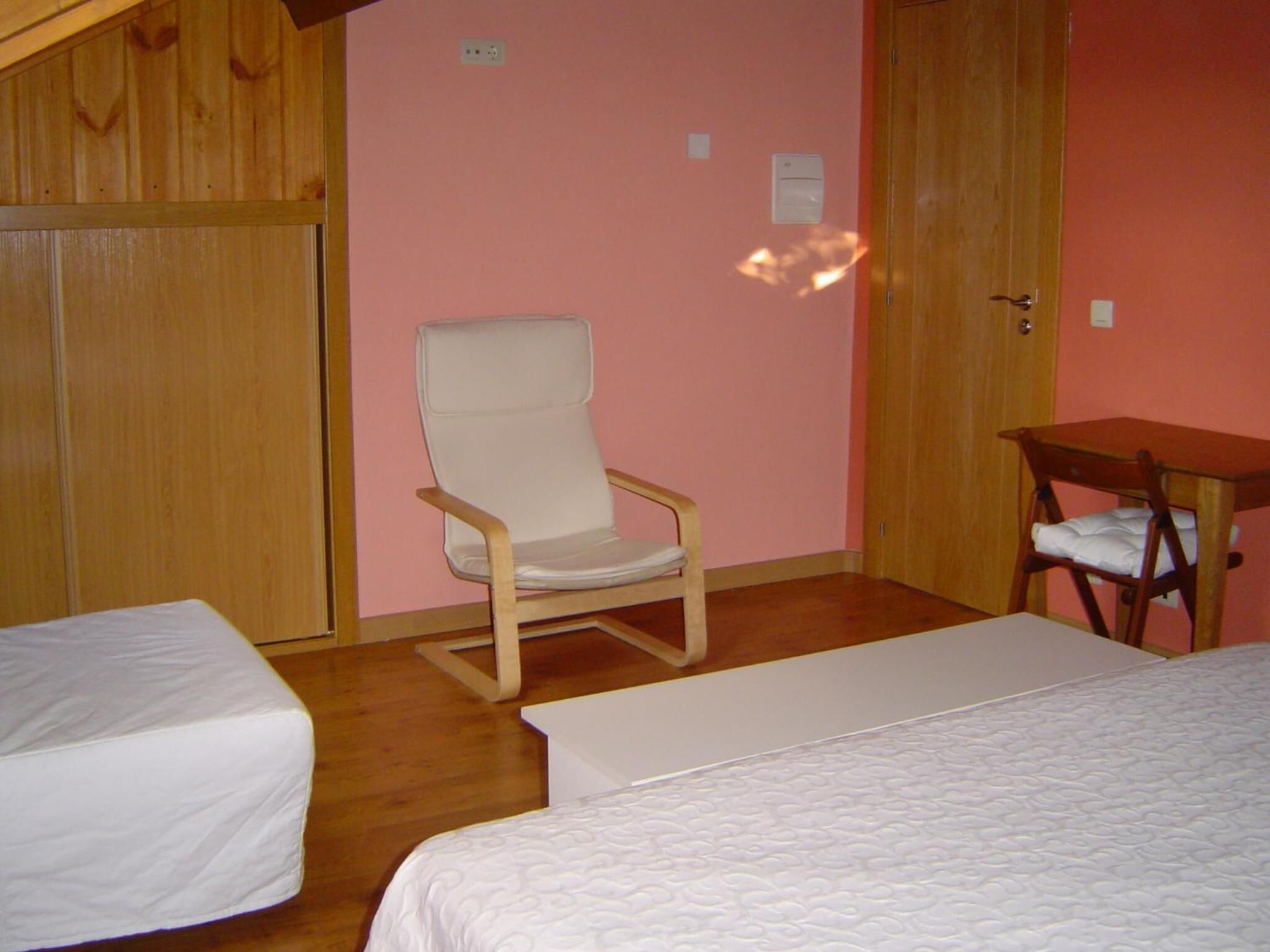 Ein Zimmer mit Holzboden, einem weißen Stuhl, zwei Betten mit weißer Bettwäsche und einem Holztisch.