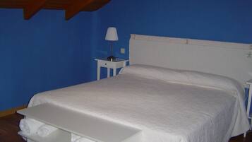 Un dormitorio con una cama individual, una mesita de noche, una lámpara y un pequeño estante con toallas.