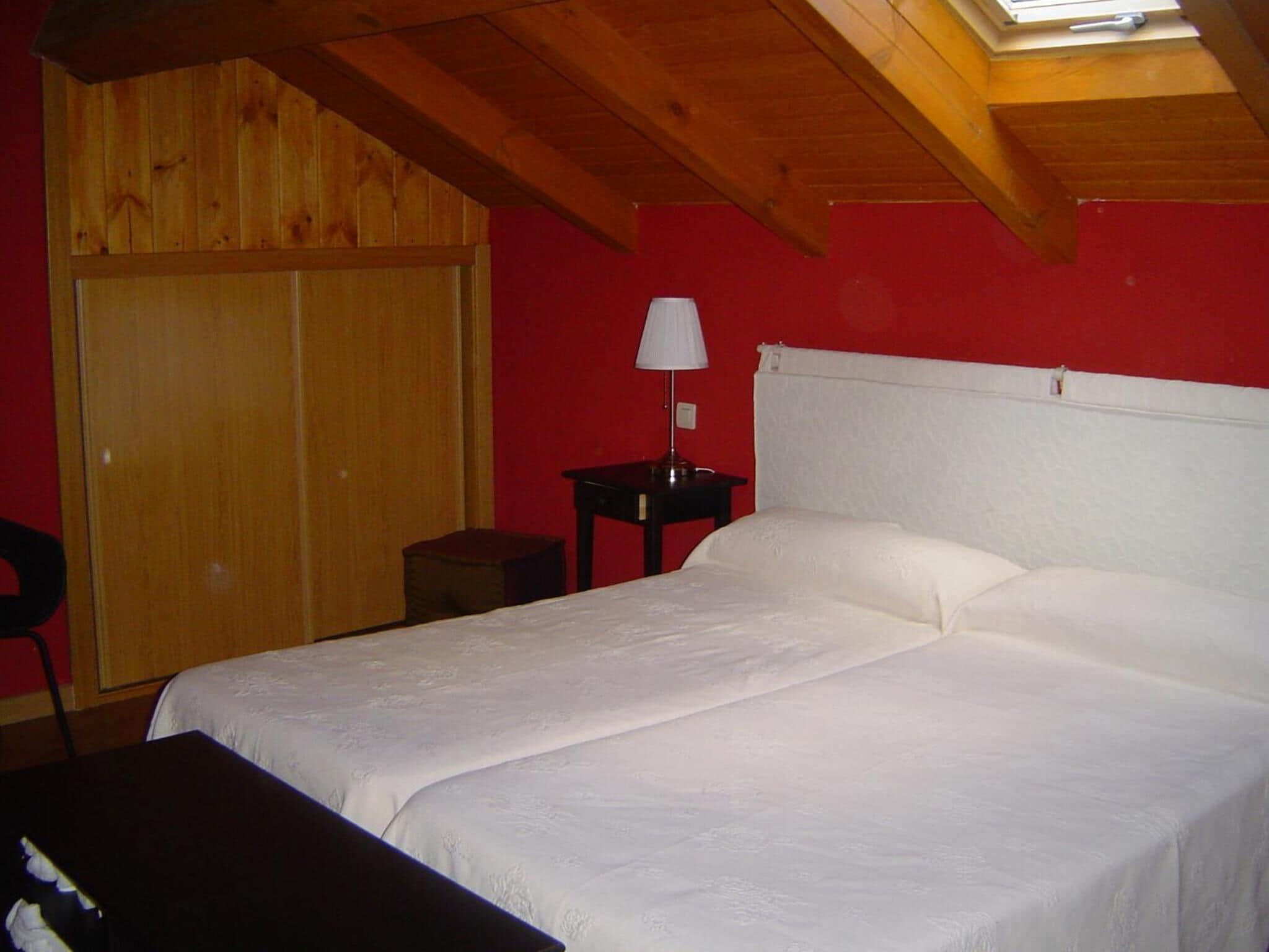 A room with a bed, a nightstand, a lamp, and a wooden wardrobe.