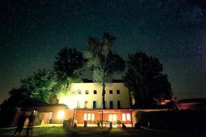 A building with a large tree in front, under a starry night sky. - Balneario de Almeida La Dama Verde (Bermillo de Sayago)