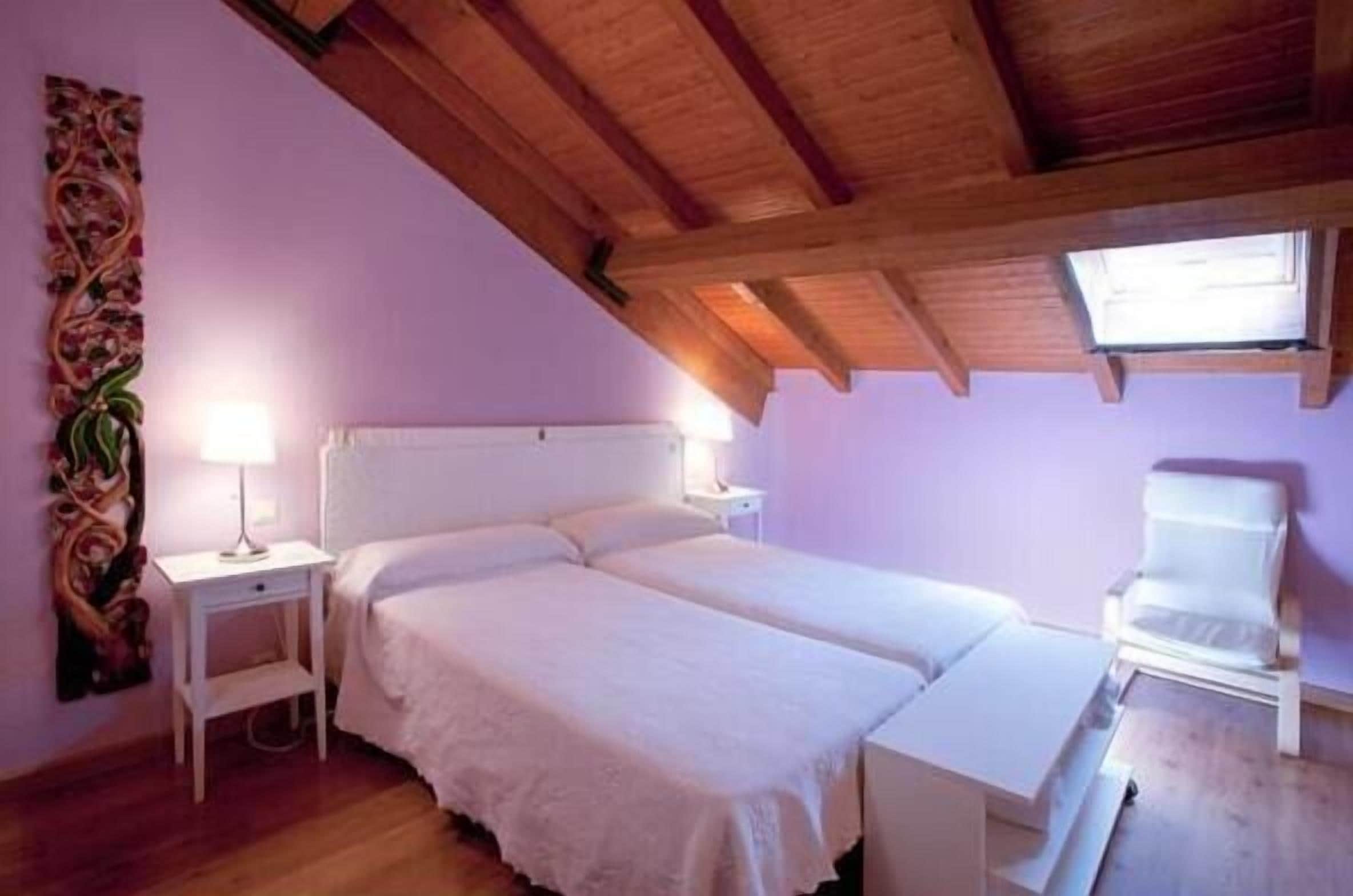 Quarto com duas camas, uma mesinha de cabeceira, uma cadeira e uma janela.