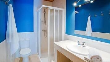Un baño con pared azul, inodoro blanco, cabina de ducha y lavabo con espejo encima.