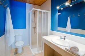 A bathroom with a blue wall, a white toilet, a shower enclosure, and a sink with a mirror above it. - Balneario de Almeida La Dama Verde (Bermillo de Sayago)