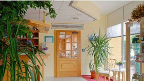 A hallway with a wooden door, a potted plant, a chair, and a glass display case. - Sporthotel Malchow (Malchow)