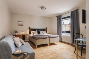 A bedroom with a bed, a sofa, a small table, a window with curtains, and a radiator. - 2Home Hotel Gävle (Gävle)