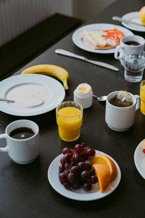 A breakfast table with plates of food, a banana, a glass of orange juice, a cup of coffee, and a bowl of soup. - 2Home Hotel Gävle (Gävle)