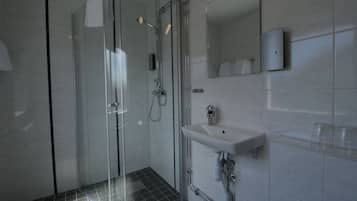 A modern bathroom with a glass-enclosed shower, a white sink, and a mirror above it.