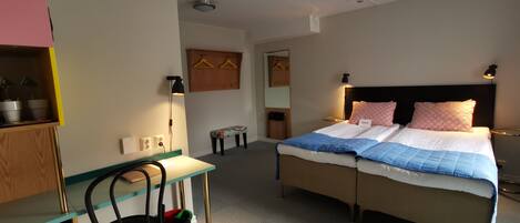 Una camera d'hotel con un letto, comodini, una scrivania, una sedia, un appendiabiti e una piccola panca.