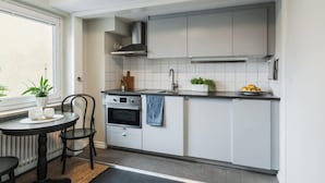Cocina pequeña con armarios blancos, horno empotrado, lavamanos y ventana con plantas.