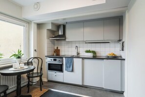 A compact kitchen with white cabinets, a built-in oven, a sink, and a window with plants. - 2Home Hotel Gävle (Gävle)