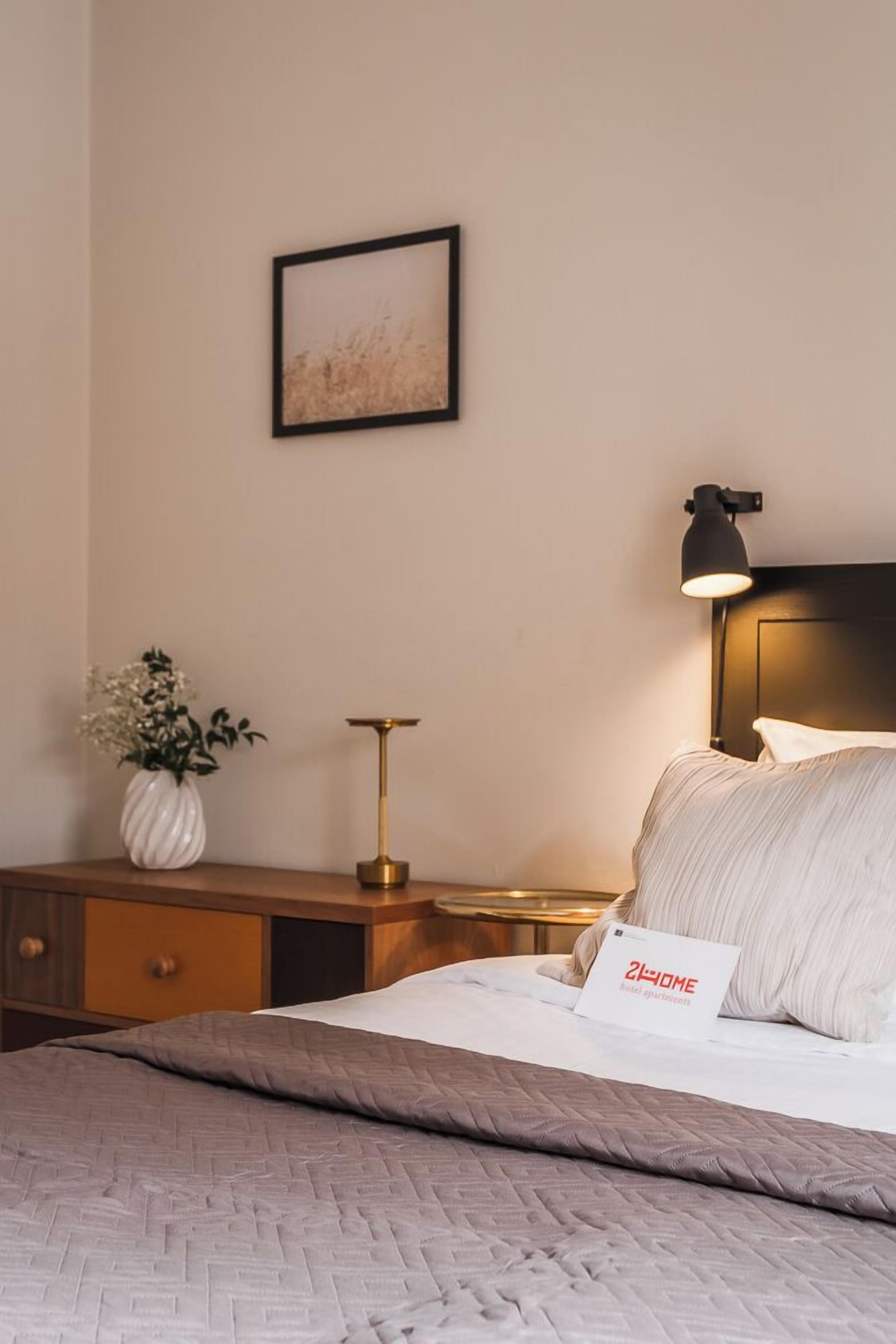 Un dormitorio ordenado con cama, mesita de noche, lámpara y un cuadro en la pared.
