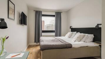 Un dormitorio con cama, un escritorio con bolígrafo, televisor y ventana con cortinas.