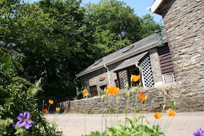 A stone building with a sloped roof and a wooden porch. - Swansea Valley Holiday Cottages (Swansea)