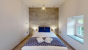 Een slaapkamer met een stenen muur, een bed met een bedspreider met een geometrisch patroon, twee kussens, een hanglamp en een raam met uitzicht.