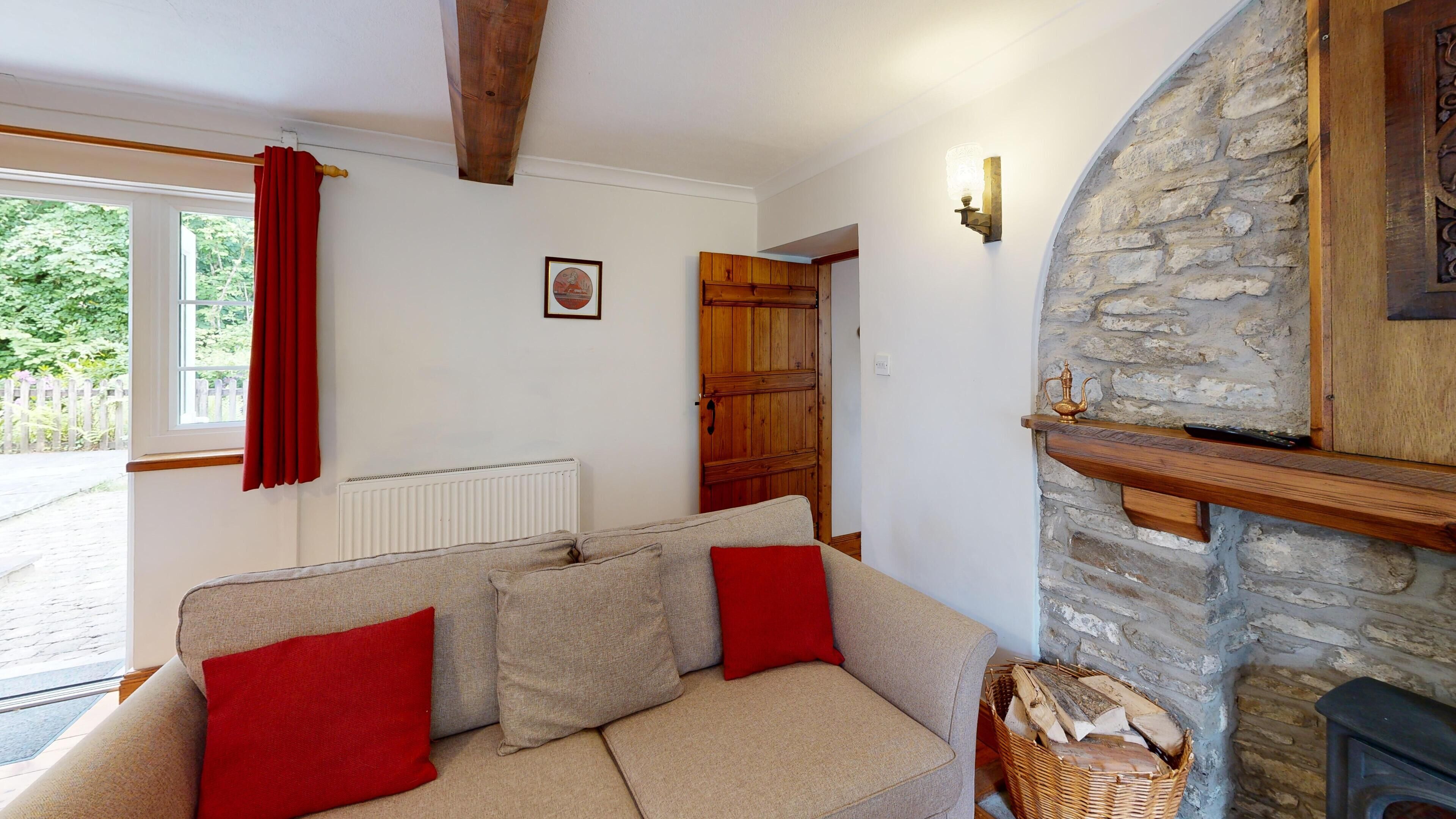 A cozy living room with a beige sofa, red cushions, a stone fireplace, and a wooden door.