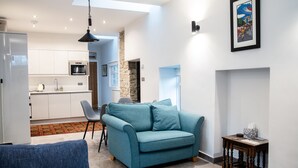 Een moderne woonkamer met een blauwe bank, een eethoek met een tafel en stoelen, en een keuken op de achtergrond.
