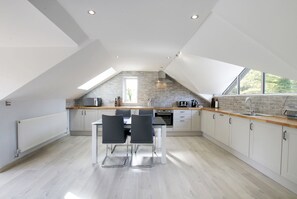 A modern kitchen with a sloped ceiling, skylight, and a dining area with a table and chairs. - Swansea Valley Holiday Cottages (Swansea)
