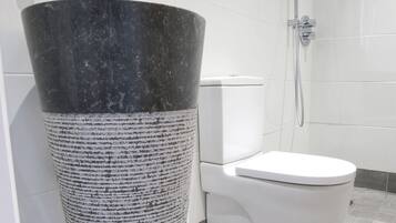 A bathroom with a large, textured sink, a toilet, and a shower.