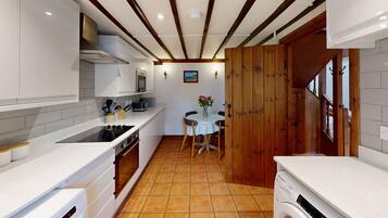 A compact kitchen with white cabinetry, a stove, and a microwave. There's a wooden door leading to another room, and a small table with chairs in the center.