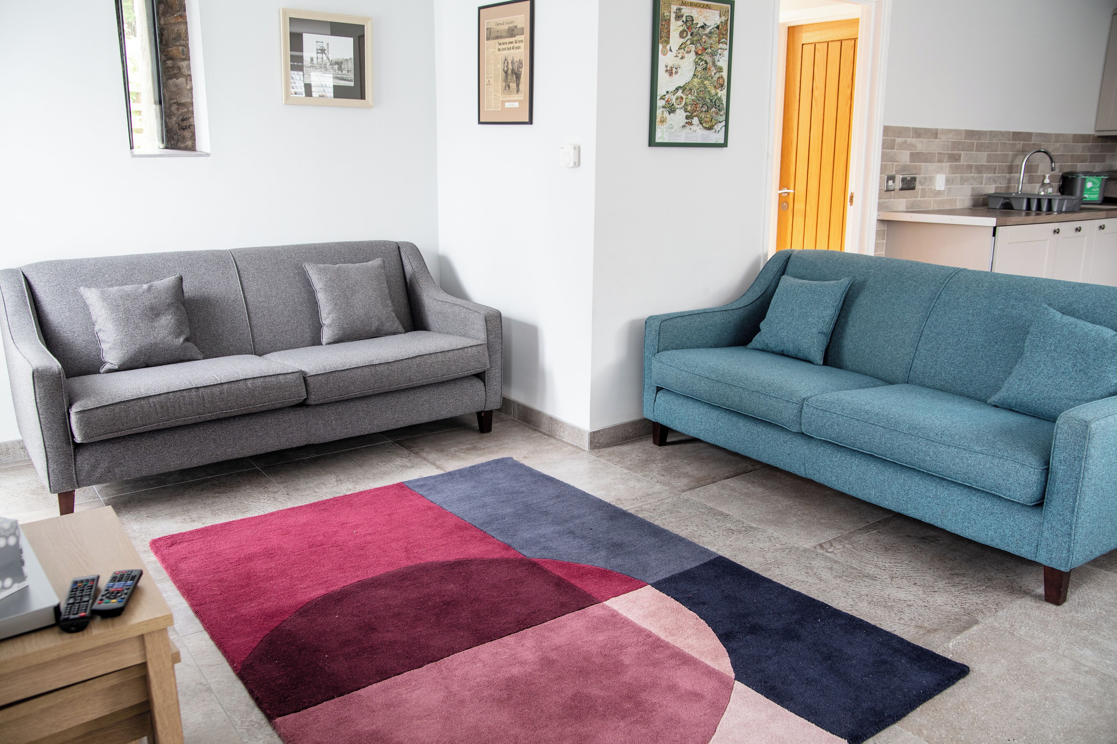 A living room with two sofas, a coffee table, and a rug. There is a kitchen area with a sink and cabinets.