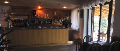 A bar area with a wooden counter, shelves with bottles, and a view of the outdoors through large windows.