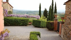 A stone building with a gravel pathway, neatly trimmed hedges, and a view of distant hills. - Fattoria di Fubbiano (Capannori)