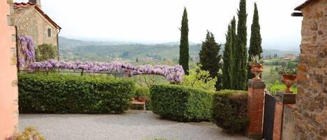 A stone building with a gravel pathway, neatly trimmed hedges, and a view of distant hills.