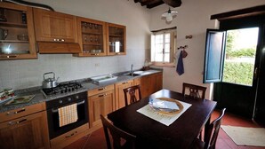 A kitchen with wooden cabinets, a gas stove, a sink, and a dining table with chairs. - Fattoria di Fubbiano (Capannori)