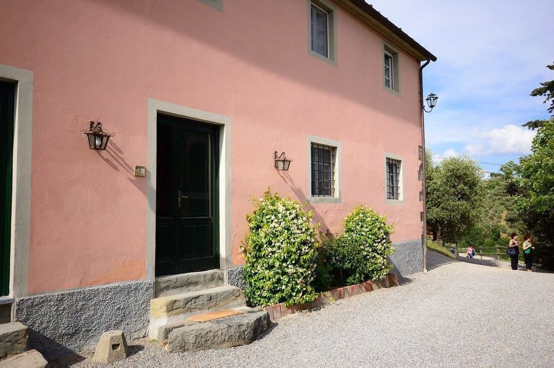 Un bâtiment rose avec une porte verte, deux fenêtres et une allée gravillonnée.