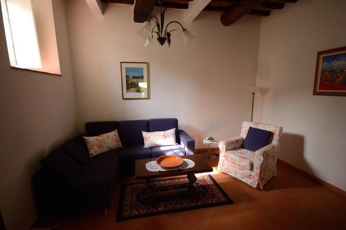 A living room with a dark blue sofa, a floral armchair, a small table with a bowl, a framed picture on the wall, and a floor lamp.