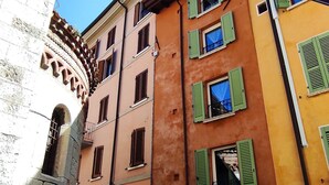 A street view with a building featuring multiple windows with green shutters, a stone archway, and a cobblestone street. - B&B Ai Musei (Brescia)
