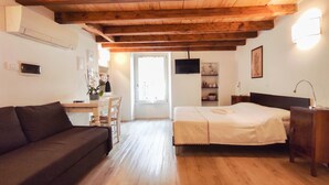 A room with a wooden ceiling, a bed, a sofa, a desk, and a TV. - B&B Ai Musei (Brescia)