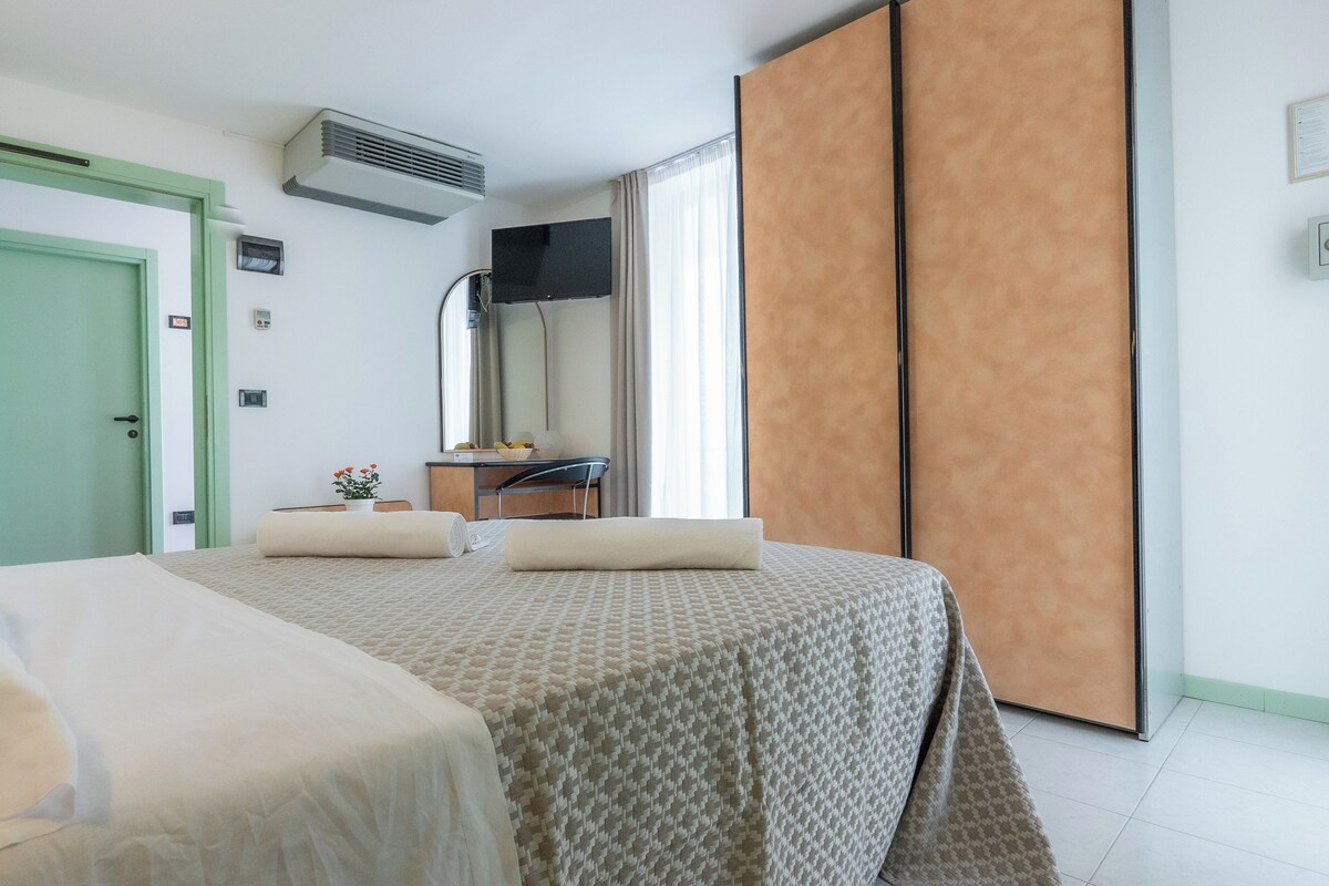 A hotel room with a bed, a desk, a chair, a TV, and a large window.