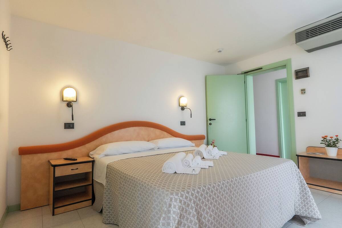 Una habitación de hotel con una cama, mesitas de noche, un escritorio y una puerta verde.