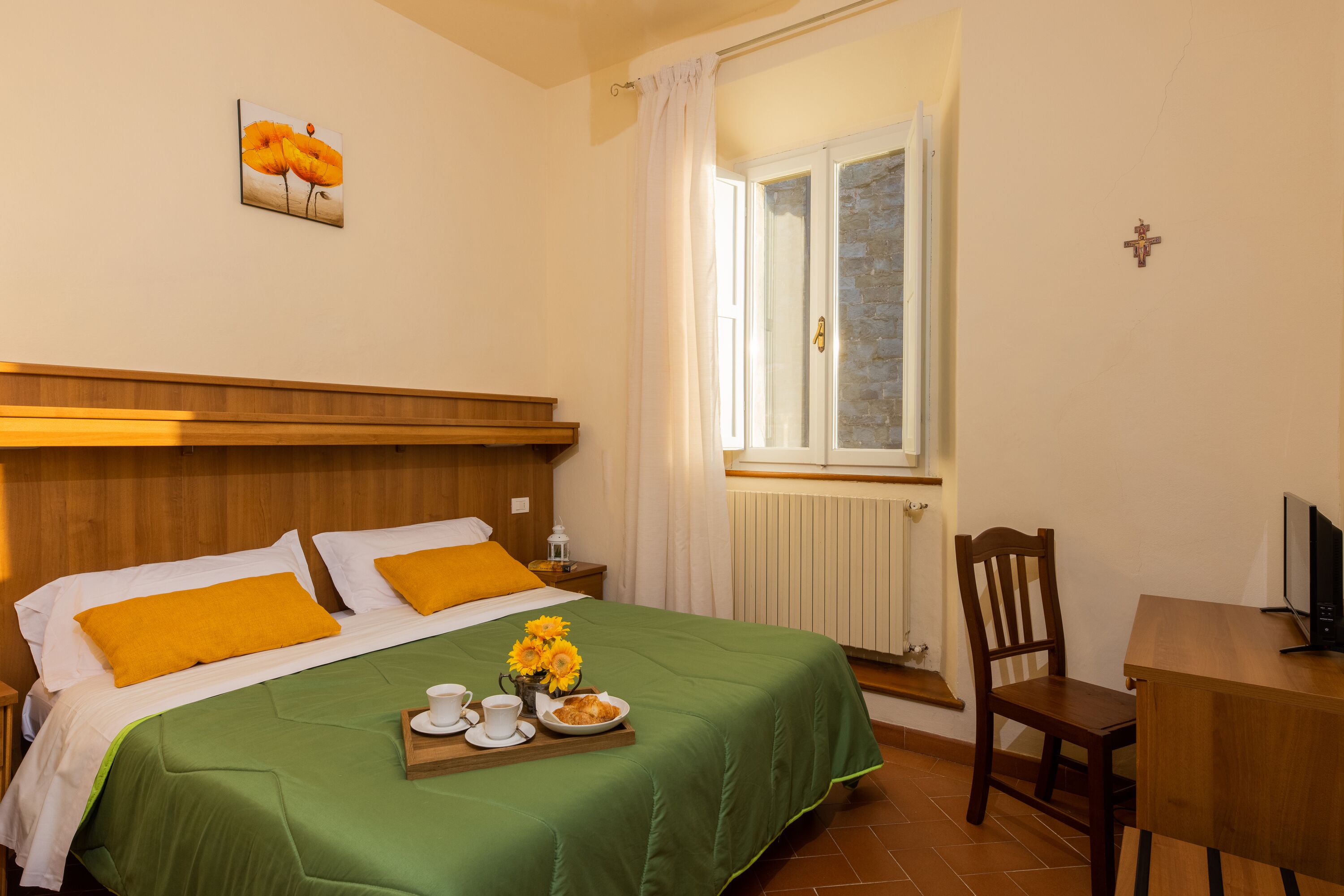 A neatly arranged bedroom with a bed, a wooden nightstand, a chair, a small table, and a television.