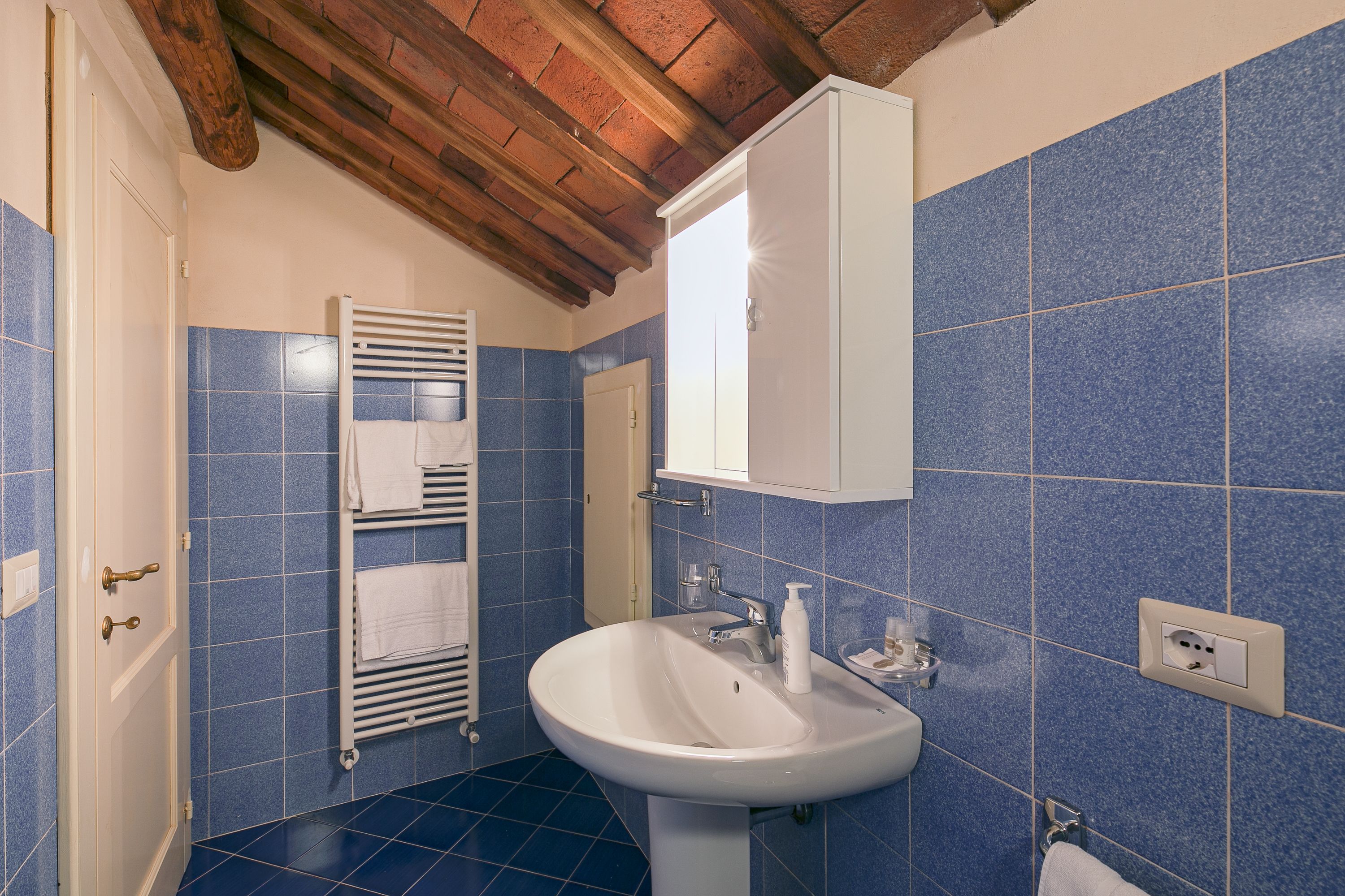 A bathroom with blue tiles, a white sink, a towel rack, and a wooden ceiling.