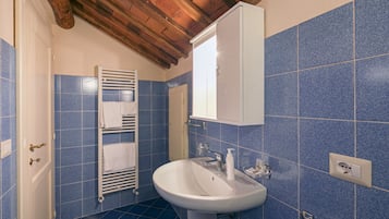 A bathroom with blue tiles, a white sink, a towel rack, and a wooden ceiling.