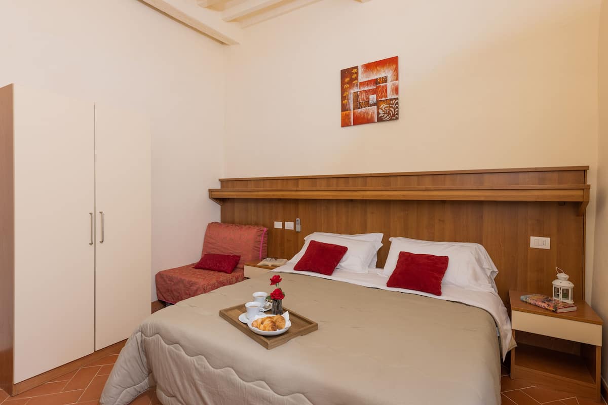 A hotel room with a bed, a chair, a nightstand, and a tray with breakfast.