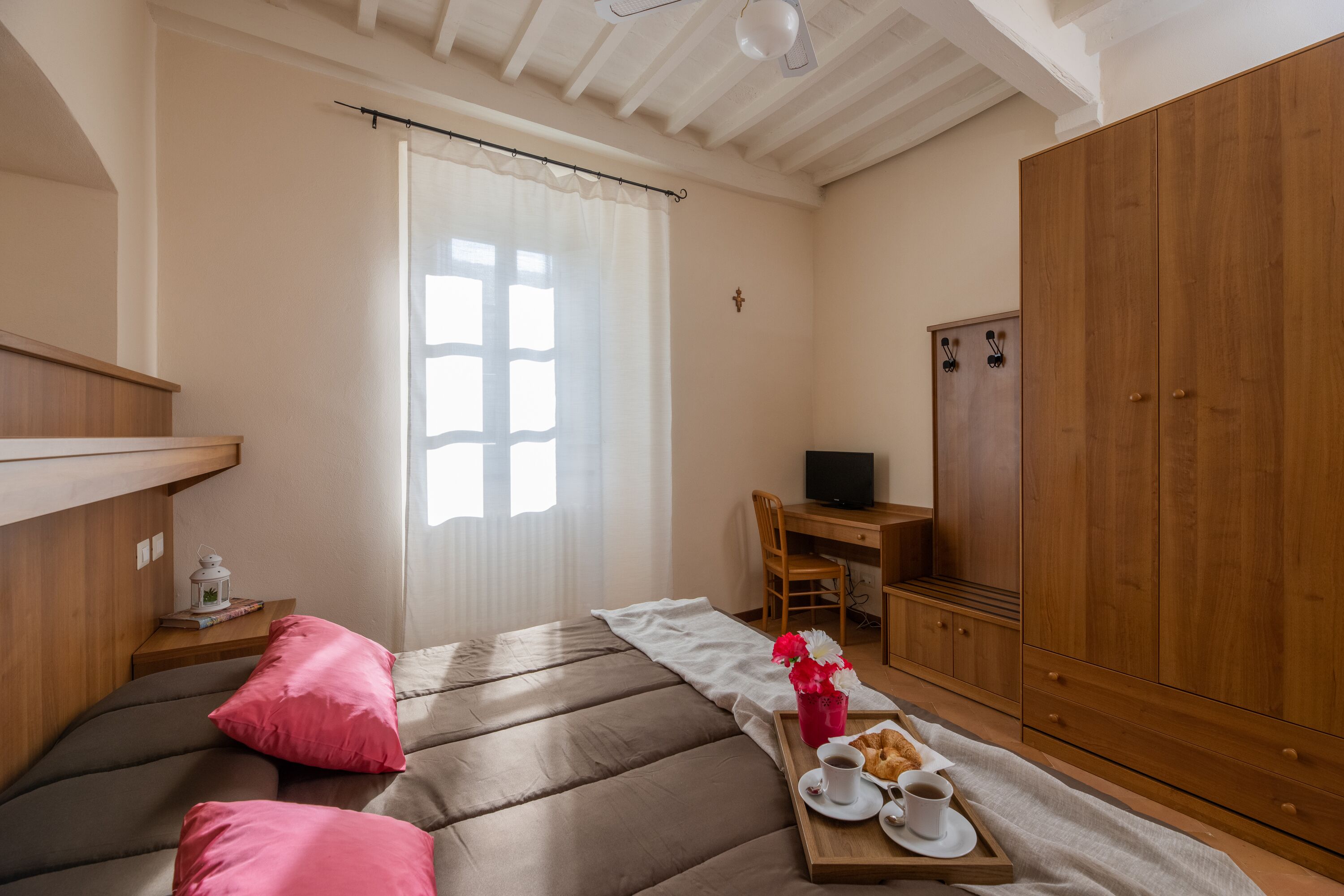 A cozy bedroom with a bed, a desk, a wardrobe, and a breakfast tray.