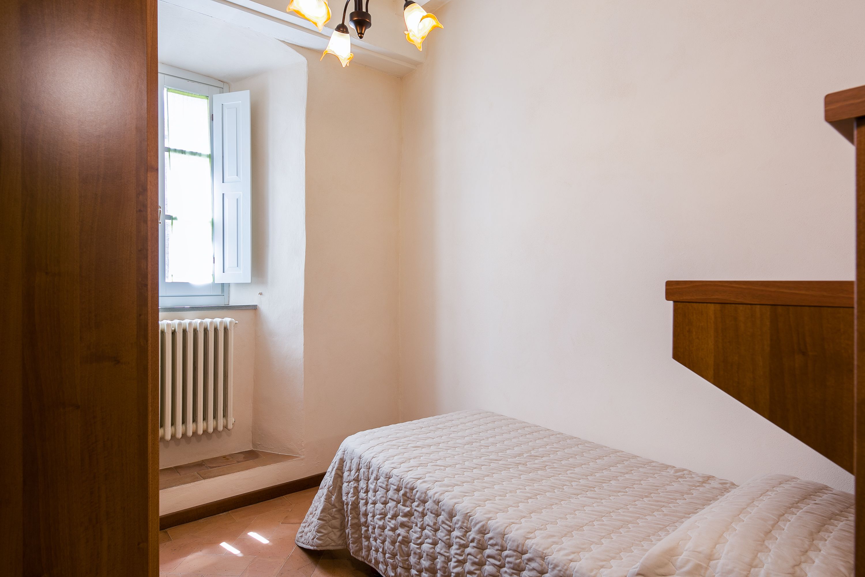 Ein Schlafzimmer mit einem Einzelbett, einem Holzkopfende, einem Fenster mit weißen Fensterläden und einer Heizung.
